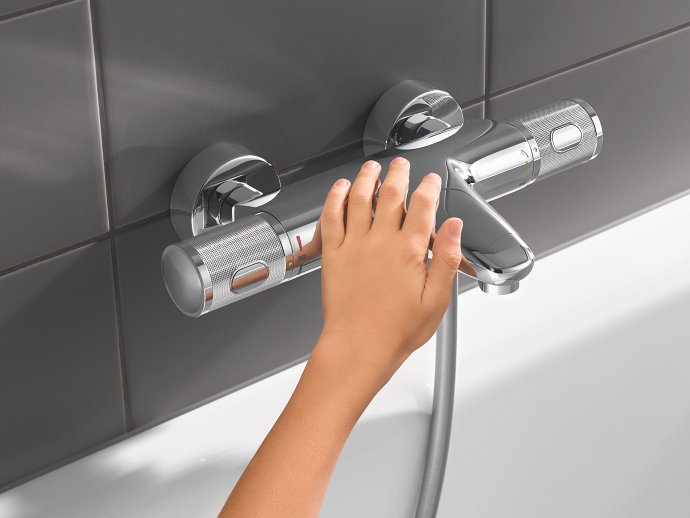 A hand touching a GROHE bath thermostat with cooltouch technology