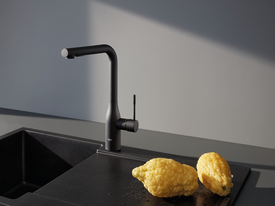 Eine elegante GROHE Küchenarmatur in Phantom Black an einem Spültisch mit Ablauf, darauf Obst. 
