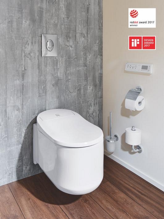 A GROHE Sensia Arena shower toilet placed above a wooden floor with many GROHE accessories attached to the wall.