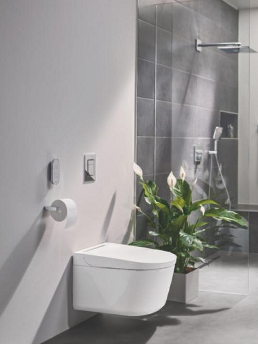 A GROHE Sensia PRO shower toilet from the side, placed in a grey bathroom with a plant next to it.