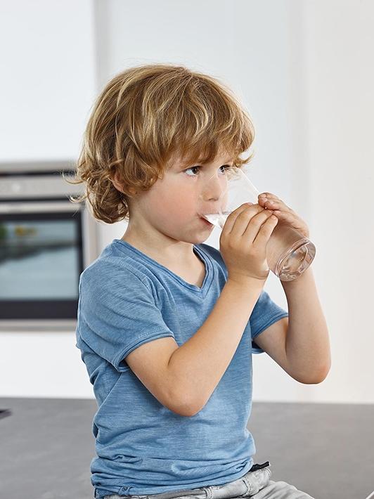 enfant qui bois un verre d'eau réfrigérée et filtrée par un système d'eau GROHE Blue