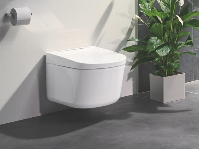 Le WC lavant japonais GROHE Sensia Pro placé dans une salle de bain blanche et grise avec une plante à côté.