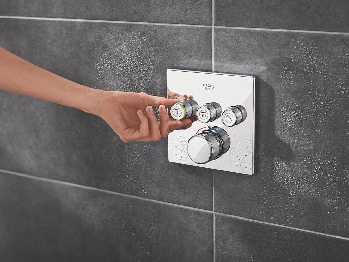 Una mano che regola la manopola del miscelatore termostatico GROHE montato su un sistema doccia a incasso. 