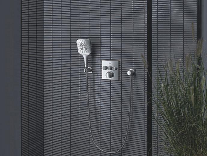 Un sistema doccia a incasso GROHE con soffione doccia e miscelatore termostatico cromato, montato su una parete piastrellata con una texture lineare.