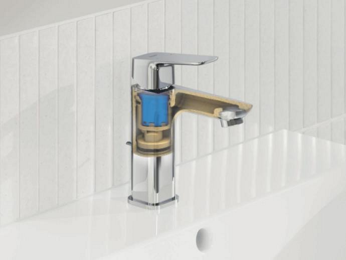 Prim-plan al unei baterii cromate GROHE Cubeo cu o vizualizare decupată care prezintă componentele interne, montat pe o chiuvetă albă cu backsplash din gresie