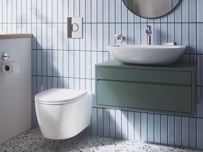 A modern bathroom interior. It features a wall-mounted white toilet, a floating sage green vanity with a white vessel sink, and a round mirror above.