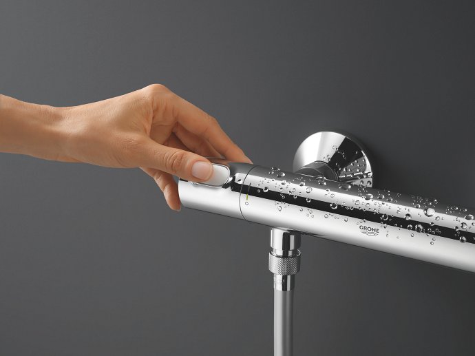 Een hand die een GROHE waterbesparende douchethermostaatkraan opent