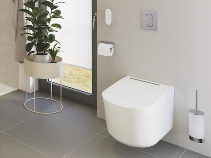 Un WC con funzione bidet GROHE Sensia in un bagno chiaro con una piastra di azionamento cromata.