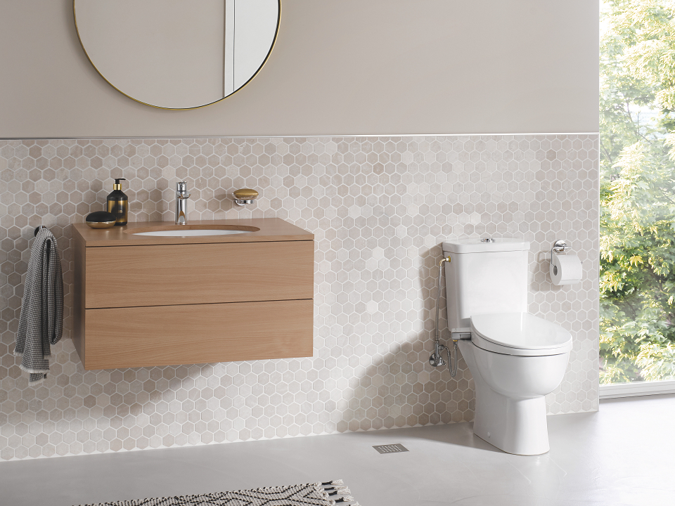 Un sedile con funzione bidet manuale collegato a un WC in un bagno beige.