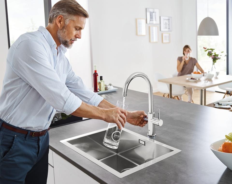 Man die een glazen karaf bijvult met kraantjeswater van GROHE Blue Home met C-uitloop